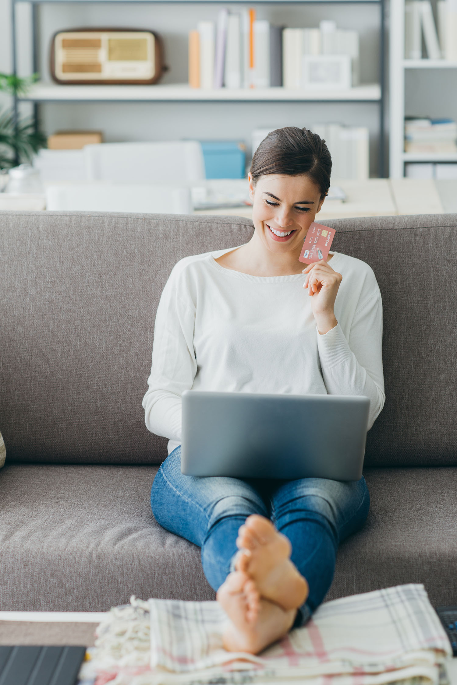 Happy woman on the sofa at home shopping online with a credit card and a laptop