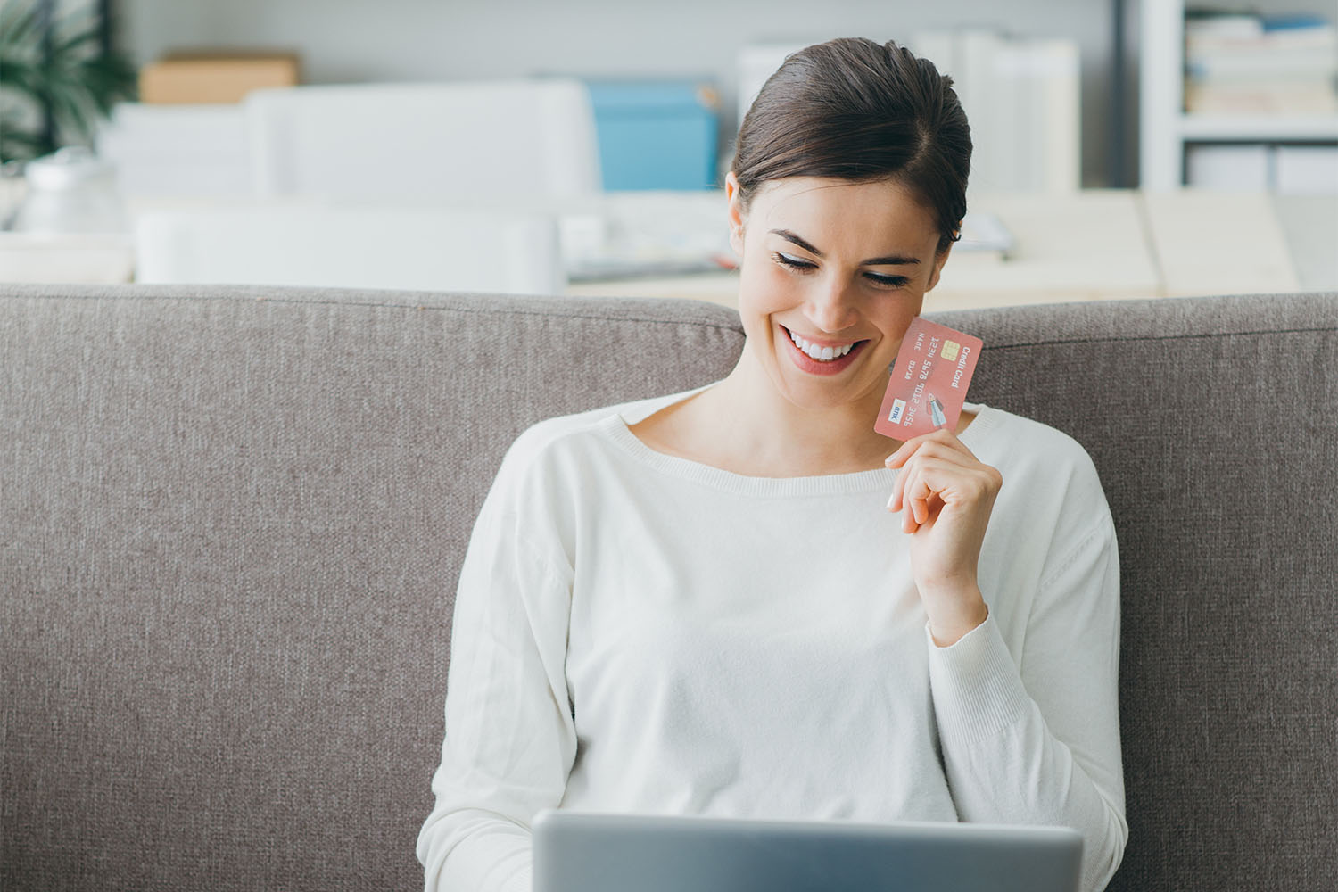 Happy woman on the sofa at home shopping online with a credit card and a laptop